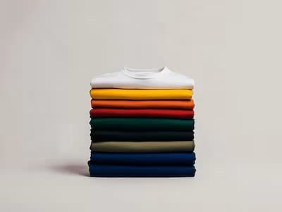 Stack of folded colorful t-shirts in various colors including white, yellow, orange, green, and blue.